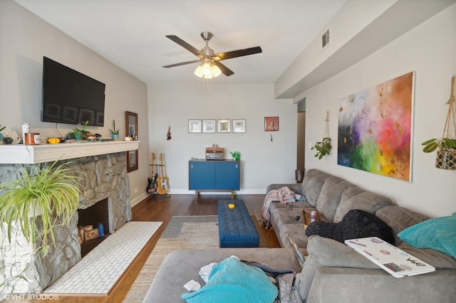 living room featuring a stone fireplace, ceiling fan, and dark hardwood / wood-style floors