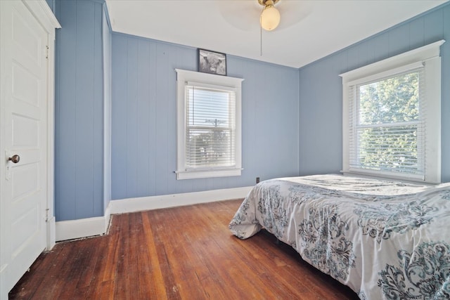 bedroom with ceiling fan, wood walls, and dark hardwood / wood-style floors