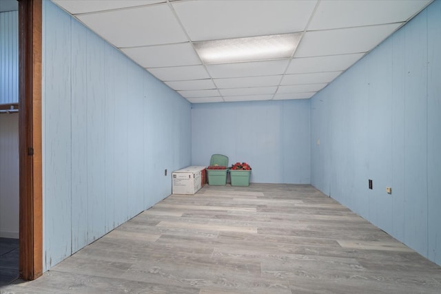 empty room featuring wooden walls, a paneled ceiling, and light wood-type flooring