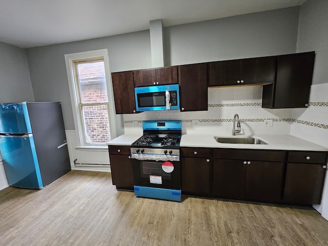 kitchen featuring appliances with stainless steel finishes, sink, backsplash, dark brown cabinetry, and light hardwood / wood-style flooring