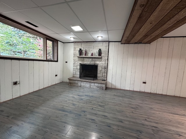 basement with a paneled ceiling, hardwood / wood-style flooring, wooden walls, and a stone fireplace