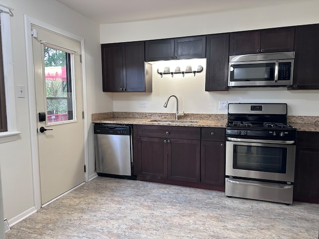 kitchen featuring dark brown cabinetry, light stone countertops, appliances with stainless steel finishes, and sink