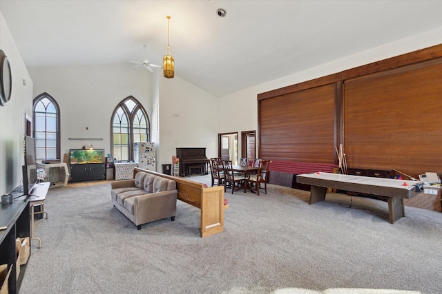 living room with light colored carpet, wooden walls, high vaulted ceiling, and ceiling fan