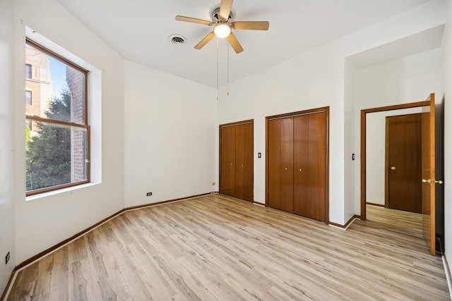 unfurnished bedroom featuring light hardwood / wood-style floors, two closets, and ceiling fan