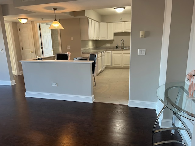 kitchen featuring sink, hardwood / wood-style floors, white cabinetry, and hanging light fixtures