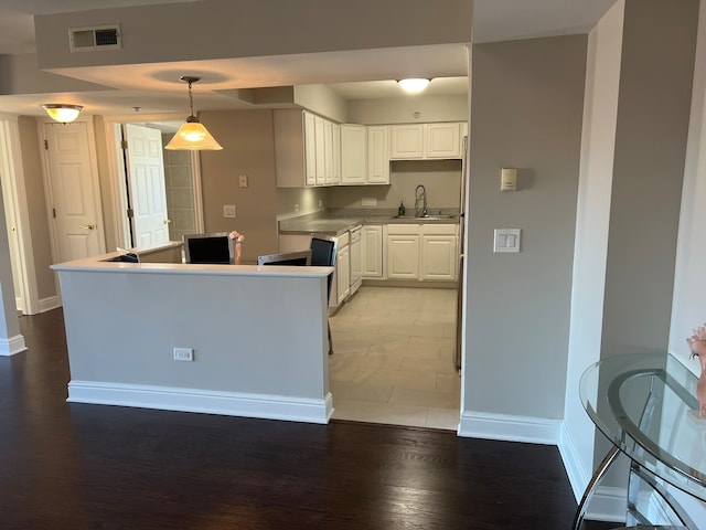 kitchen with sink, light hardwood / wood-style floors, decorative light fixtures, and white cabinets