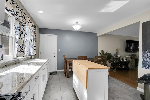 kitchen featuring light stone countertops, light wood-type flooring, a kitchen island, black stove, and white cabinetry