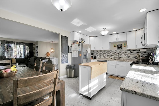 kitchen featuring a kitchen island, backsplash, light stone countertops, pendant lighting, and white cabinetry