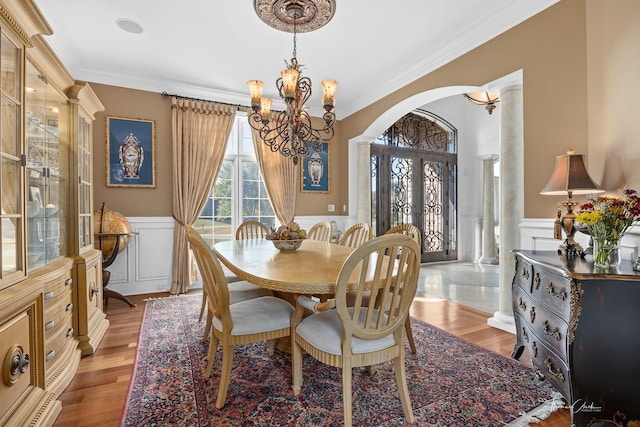 dining room featuring ornate columns, ornamental molding, an inviting chandelier, and light wood-type flooring