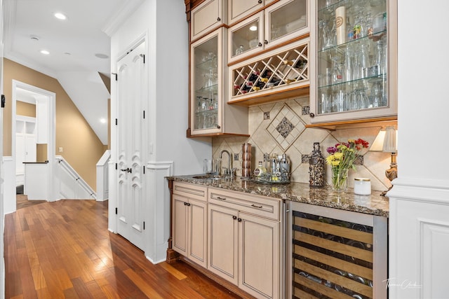 bar featuring tasteful backsplash, sink, dark stone countertops, beverage cooler, and dark wood-type flooring