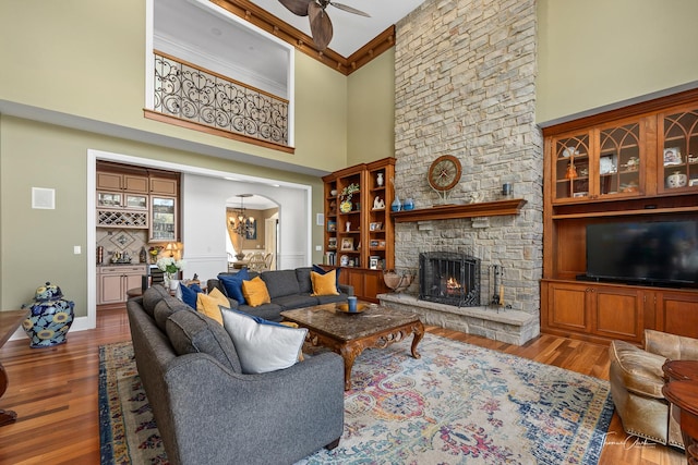 living room with a stone fireplace, a towering ceiling, ceiling fan with notable chandelier, and light wood-type flooring