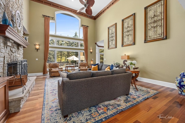 living room featuring a stone fireplace, light hardwood / wood-style flooring, ceiling fan, and a high ceiling