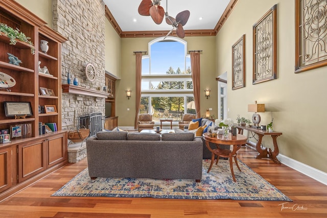 living room featuring crown molding, a towering ceiling, a fireplace, and light hardwood / wood-style floors