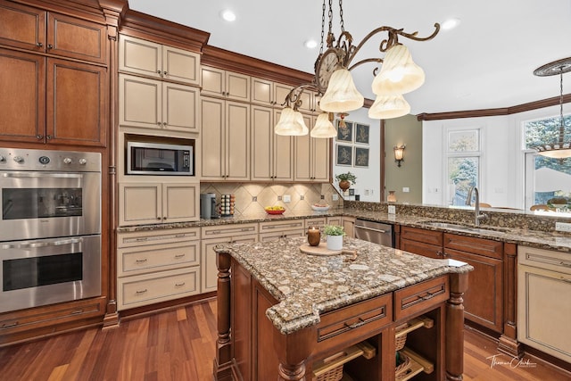 kitchen with sink, a center island, appliances with stainless steel finishes, pendant lighting, and cream cabinetry