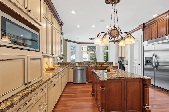 kitchen featuring decorative light fixtures, ornamental molding, appliances with stainless steel finishes, kitchen peninsula, and a kitchen island