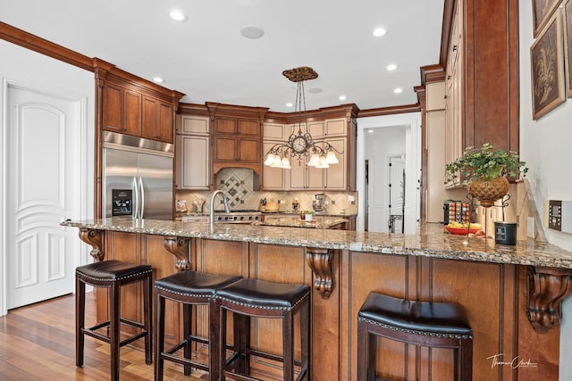 kitchen featuring sink, hardwood / wood-style floors, stainless steel built in refrigerator, stone countertops, and kitchen peninsula