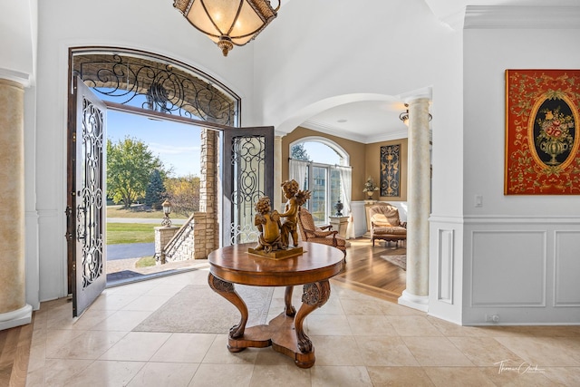 entryway with light tile patterned floors, ornamental molding, decorative columns, and a high ceiling