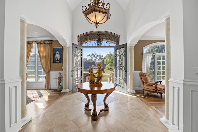 tiled foyer featuring ornamental molding, high vaulted ceiling, and ornate columns