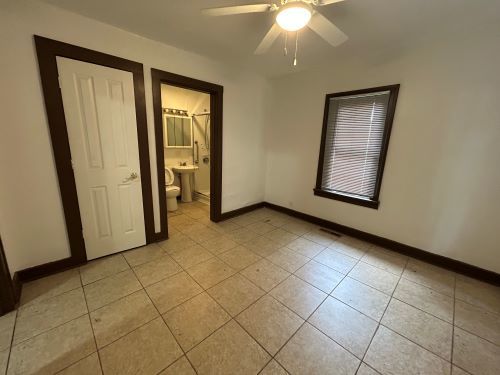 unfurnished bedroom featuring ensuite bathroom, light tile patterned floors, and ceiling fan