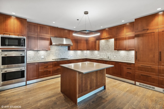 kitchen featuring stainless steel appliances, light hardwood / wood-style floors, decorative backsplash, and a center island