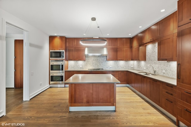 kitchen featuring stainless steel appliances, a center island, hanging light fixtures, sink, and light wood-type flooring