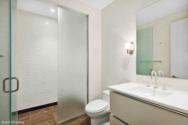 bathroom with tile walls, vanity, toilet, and a shower with door