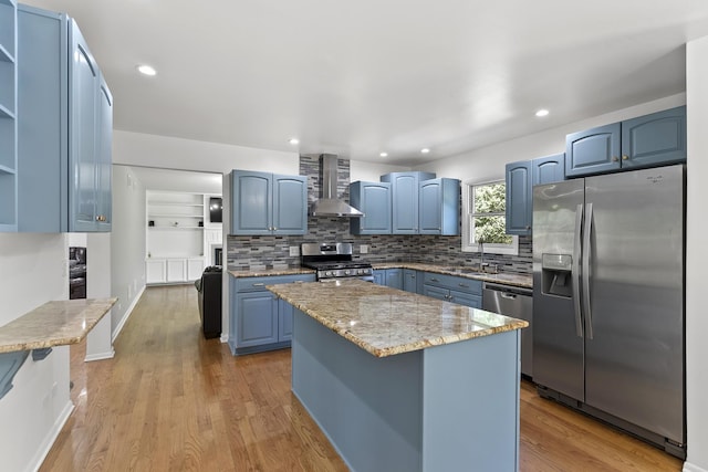 kitchen featuring wall chimney exhaust hood, blue cabinetry, sink, and stainless steel appliances