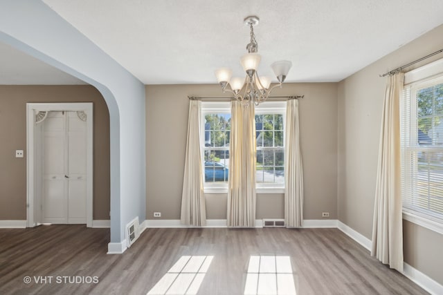 unfurnished dining area featuring hardwood / wood-style floors, a textured ceiling, and a notable chandelier