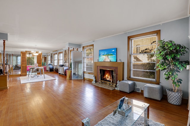 living room featuring ornamental molding, hardwood / wood-style floors, a chandelier, and a brick fireplace