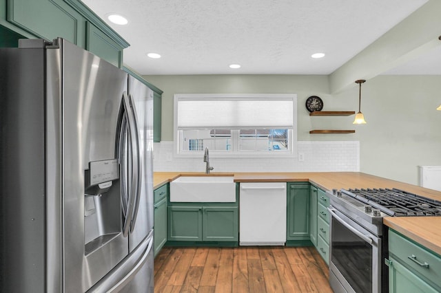 kitchen with wood counters, sink, green cabinetry, decorative light fixtures, and stainless steel appliances