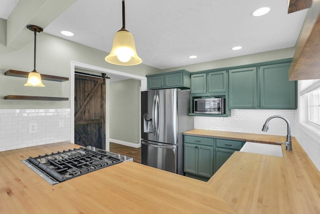 kitchen featuring wooden counters, hanging light fixtures, green cabinetry, stainless steel appliances, and a barn door