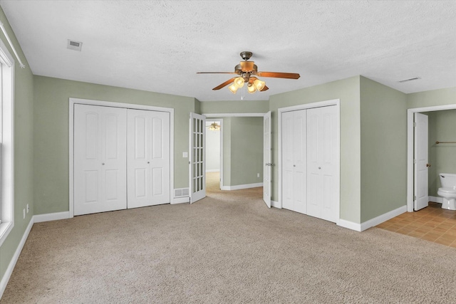 unfurnished bedroom with ceiling fan, ensuite bath, light carpet, and a textured ceiling