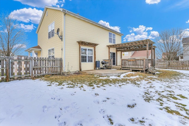 snow covered rear of property with a wooden deck and a pergola