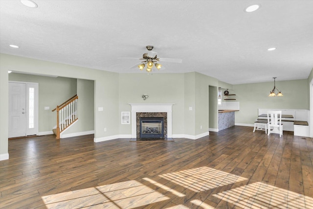 unfurnished living room with ceiling fan with notable chandelier, a textured ceiling, a fireplace, and dark hardwood / wood-style flooring