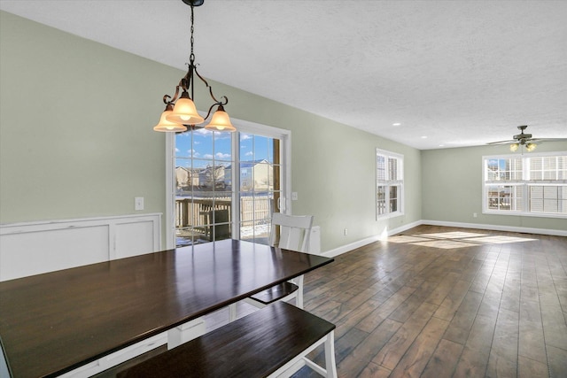 unfurnished dining area with a healthy amount of sunlight, ceiling fan with notable chandelier, dark hardwood / wood-style floors, and a textured ceiling