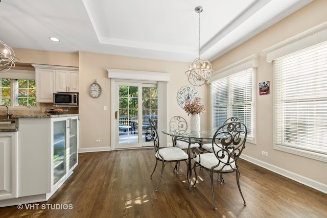 dining space featuring dark hardwood / wood-style floors, a raised ceiling, and a notable chandelier