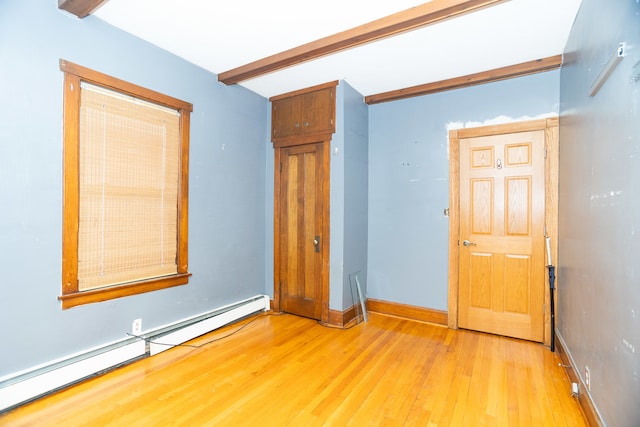 unfurnished bedroom with beam ceiling, a baseboard heating unit, and light wood-type flooring