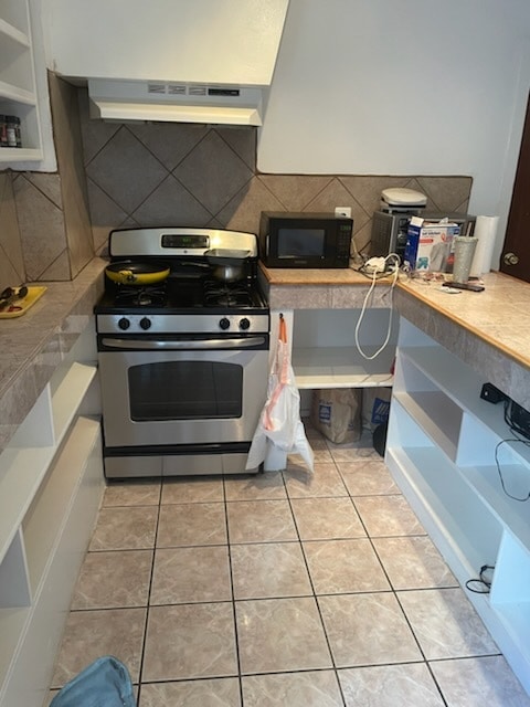 kitchen featuring decorative backsplash, stainless steel gas range oven, white cabinets, extractor fan, and light tile patterned flooring