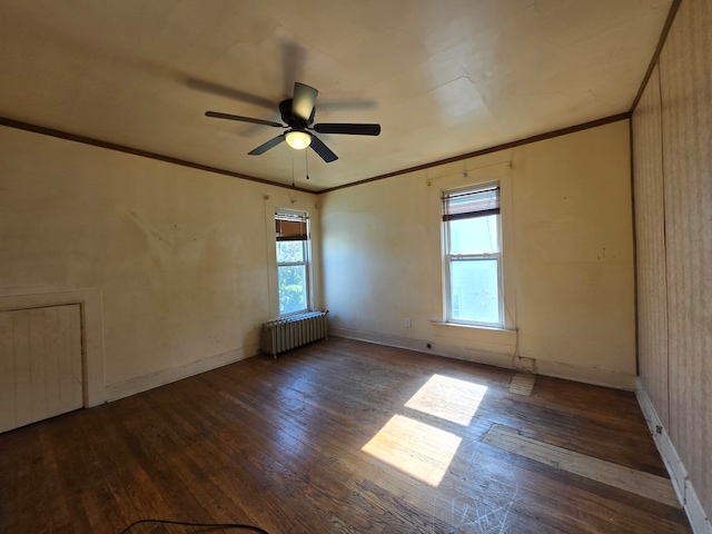 spare room with dark wood-type flooring, a healthy amount of sunlight, radiator, and ceiling fan