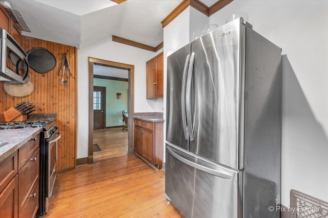 kitchen featuring crown molding, light hardwood / wood-style flooring, appliances with stainless steel finishes, wooden walls, and stone counters