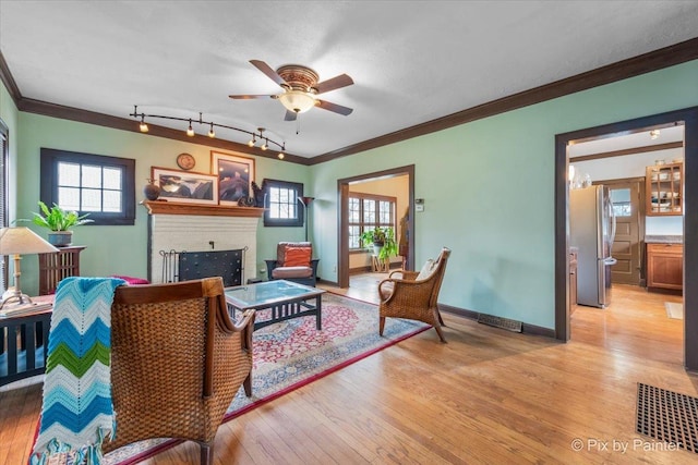 living room with rail lighting, ceiling fan, ornamental molding, light hardwood / wood-style floors, and a brick fireplace