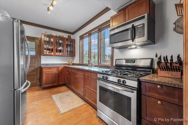 kitchen featuring appliances with stainless steel finishes, sink, dark stone countertops, ornamental molding, and light hardwood / wood-style floors