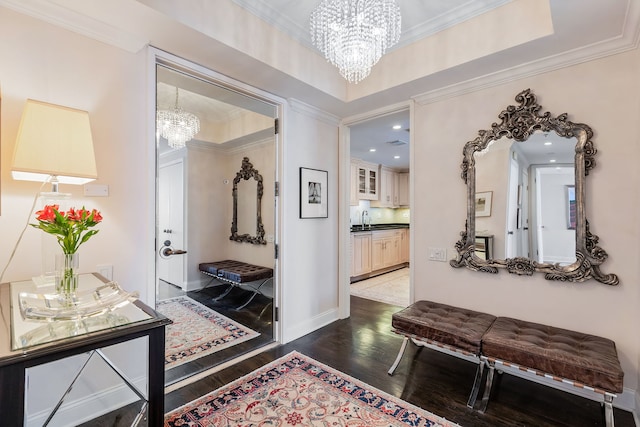 corridor with sink, a tray ceiling, crown molding, dark wood-type flooring, and an inviting chandelier