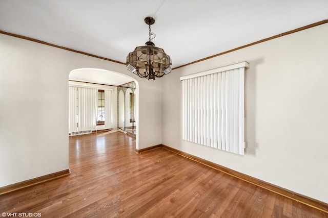 spare room featuring wood-type flooring, ornamental molding, and a notable chandelier