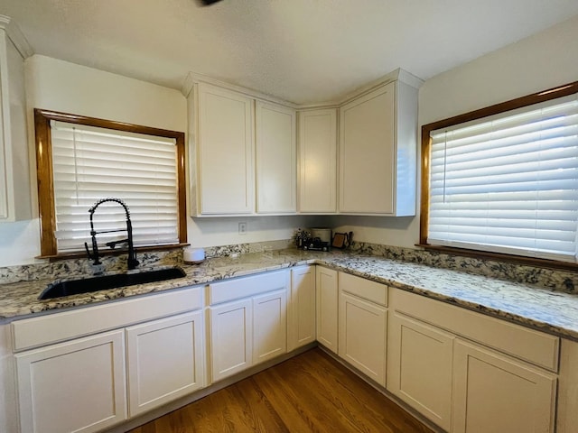 kitchen with light stone counters, wood-type flooring, sink, and white cabinets