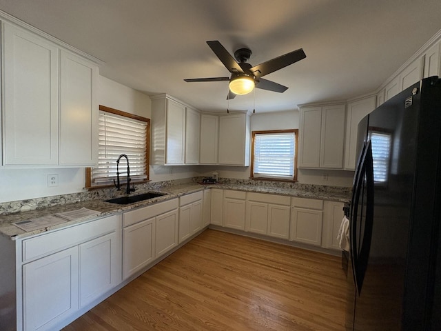 kitchen featuring sink, white cabinetry, light stone counters, light hardwood / wood-style floors, and black fridge