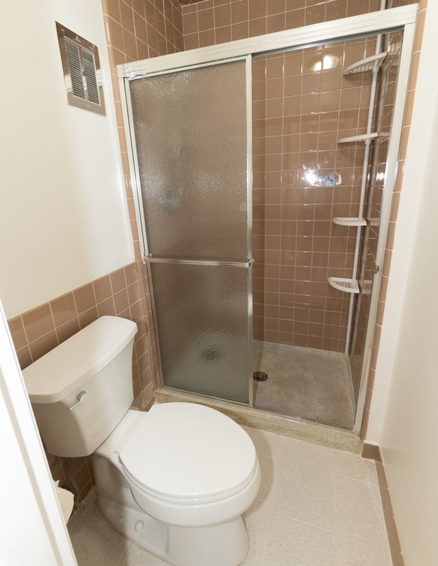 bathroom with tile patterned floors, toilet, tile walls, and walk in shower