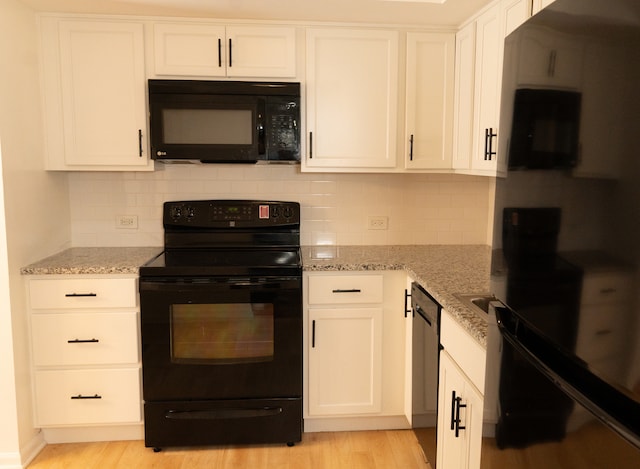 kitchen with light stone countertops, white cabinets, black appliances, and light hardwood / wood-style floors