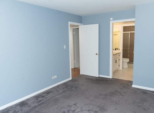 unfurnished bedroom with connected bathroom and dark colored carpet