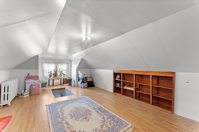 bonus room featuring lofted ceiling, hardwood / wood-style flooring, and radiator